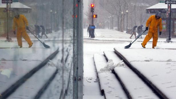 Eine Person in gelber Kleidung schaufelt Schnee auf einer verschneiten Straße.