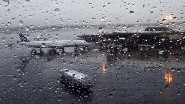 Blick durch ein verregnetes Fenster auf ein Flugzeug am Flughafen.