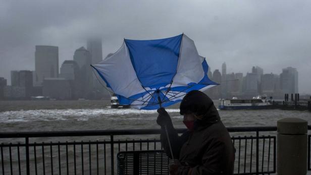 Eine Person hält einen Regenschirm bei stürmischem Wetter mit der Skyline von New York im Hintergrund.