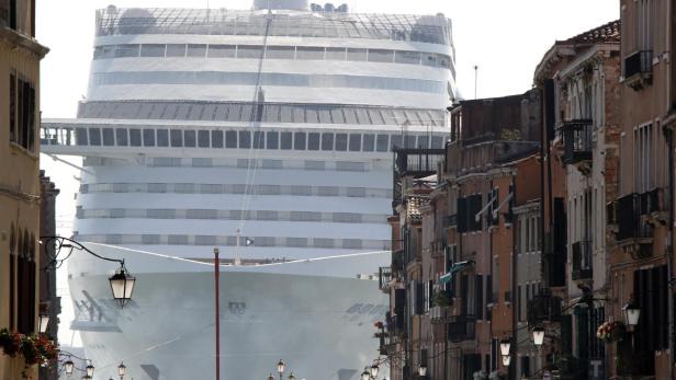 Ein großes Kreuzfahrtschiff ragt hinter den Gebäuden einer venezianischen Straße auf.