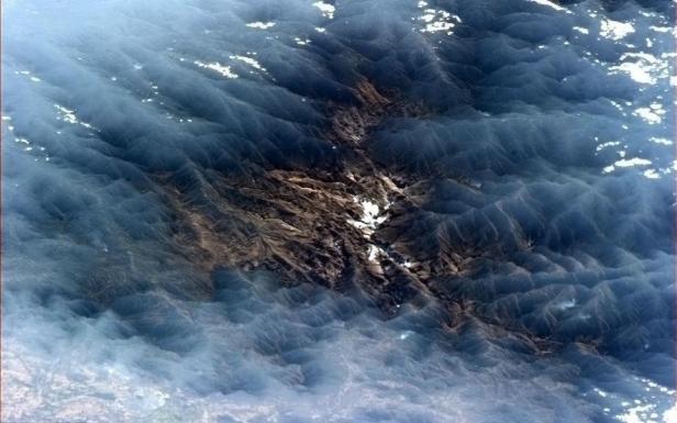 Luftaufnahme einer bergigen Landschaft mit vereinzelten Schneeflecken.