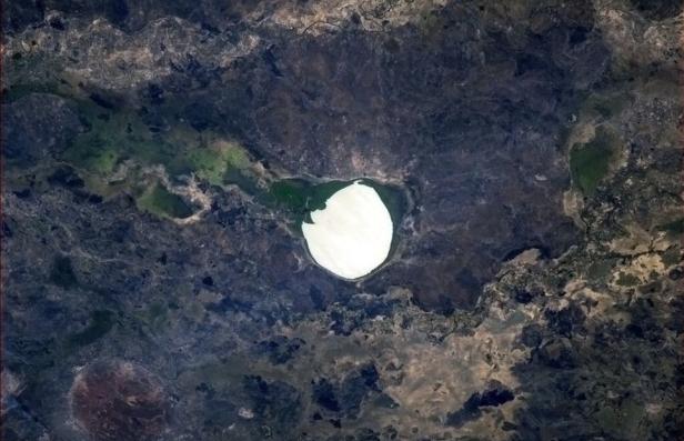Satellitenansicht eines strahlend weißen Sees, umgeben von dunkler, zerklüfteter Landschaft.