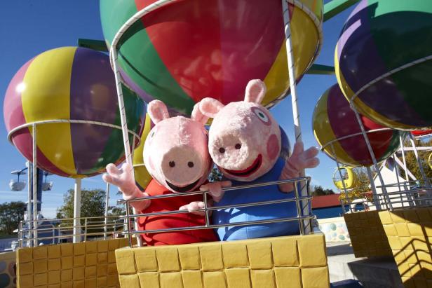 Zwei Peppa Pig-Figuren in einem bunten Heißluftballon auf einem Themenparkgelände.