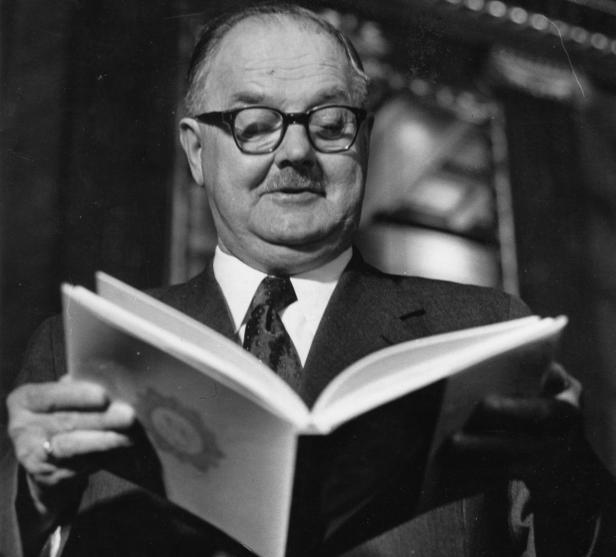 Ein Mann mit Brille und Anzug liest in einem aufgeschlagenen Buch.