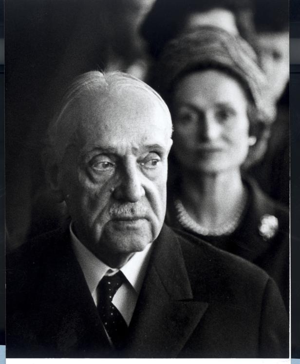 Schwarzweißporträt von Konrad Adenauer mit einer Frau im Hintergrund.