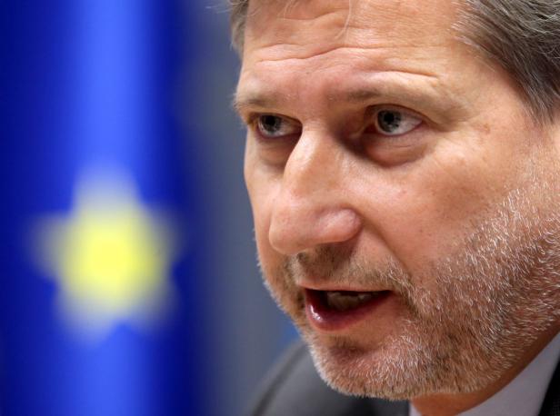 Ein Mann spricht vor einer blau-gelben Flagge.