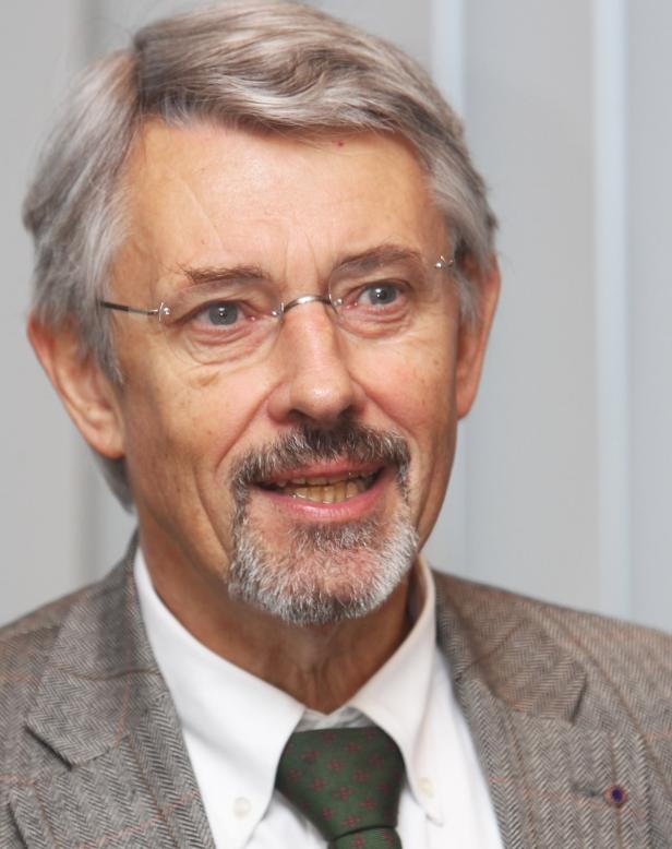 Porträt eines lächelnden Mannes mit Brille, Bart und grauem Haar.