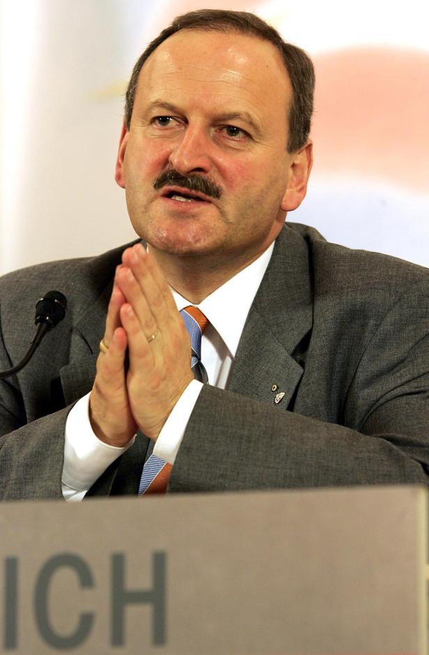 Ein Mann im Anzug mit gefalteten Händen vor einem Mikrofon.