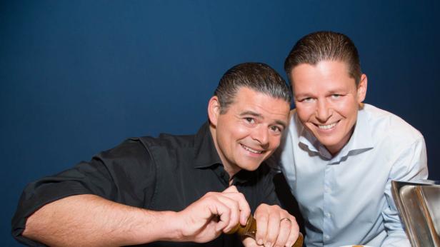 Zwei lächelnde Männer posieren, einer mit einer Pfeffermühle in der Hand.