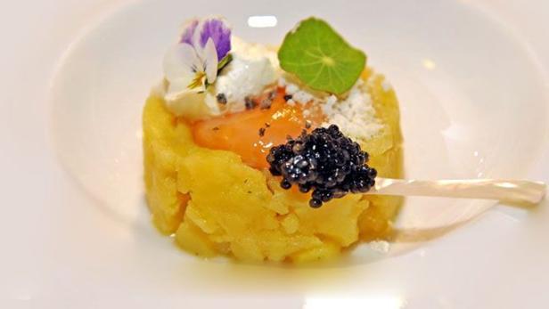 Ein Kartoffelgericht mit Kaviar, Ei und essbaren Blüten auf einem weißen Teller.