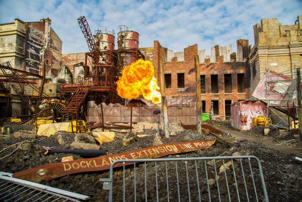 Eine Explosion vor einer zerstörten Industriekulisse mit dem Schriftzug „Docklands Extension Line Project“.