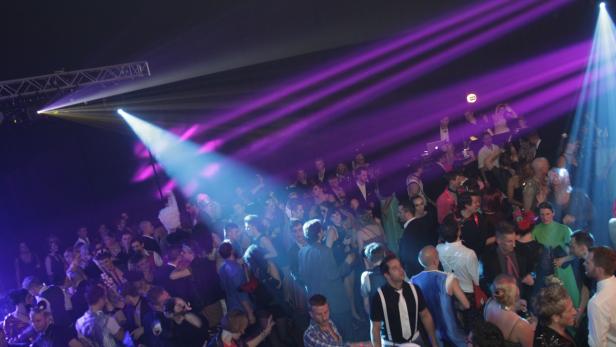 Eine große Menschenmenge tanzt unter farbigen Scheinwerfern auf einer Party.