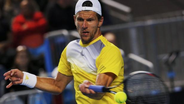 Ein Tennisspieler in gelbem Hemd schlägt einen Tennisball.