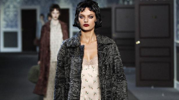 Eine Frau mit dunklem Haar und dunklem Mantel auf einem Laufsteg.