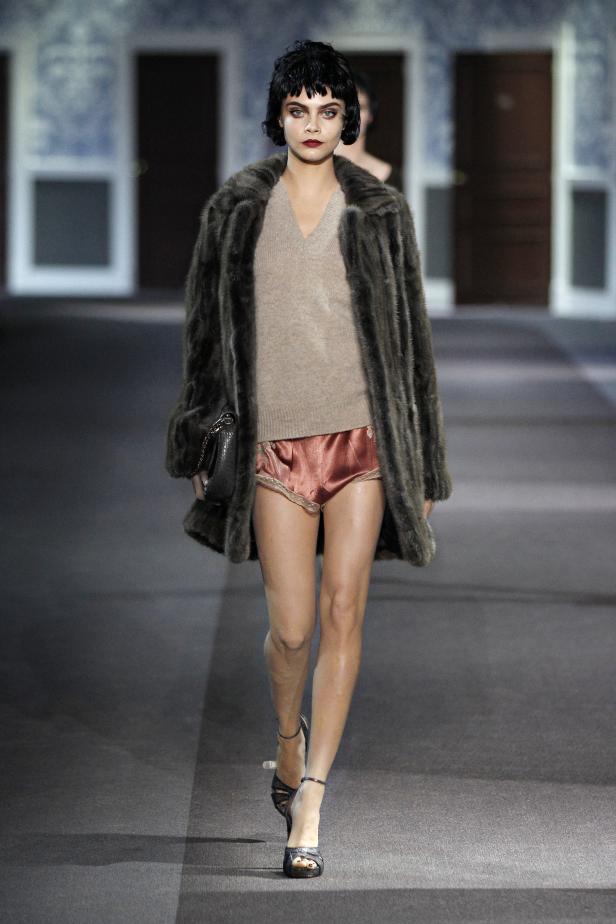 Cara Delevingne läuft in einem Pelzmantel und Shorts über einen Laufsteg.