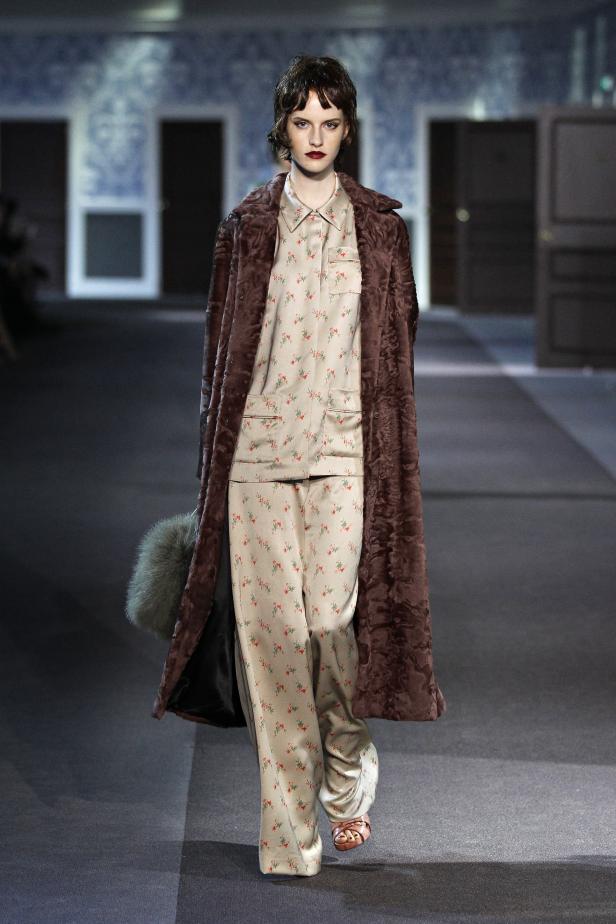 Eine Frau in einem floralen Pyjama und einem braunen Mantel auf einem Laufsteg.