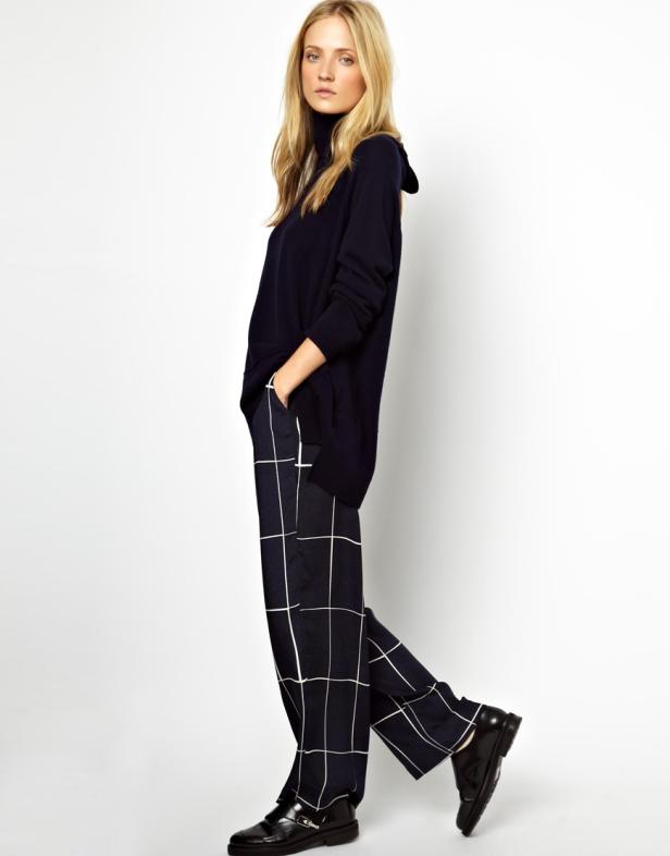 Eine blonde Frau posiert in einem marineblauen Rollkragenpullover und einer karierten Hose.