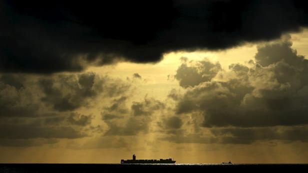 Ein Containerschiff fährt unter einem dramatischen, bewölkten Himmel auf dem Meer.
