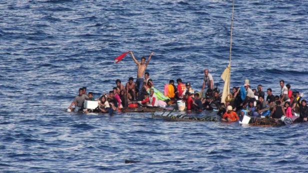 Eine Gruppe von Menschen sitzt auf einem provisorischen Floß mitten auf dem Meer.