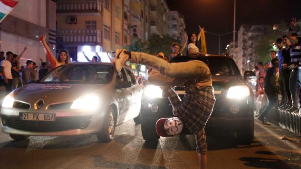 Eine Person mit Guy-Fawkes-Maske macht einen Handstand auf einer belebten Straße.