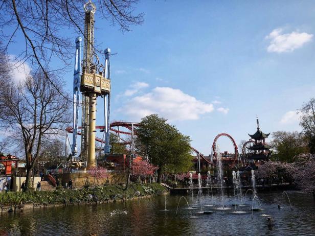 Blick auf den Tivoli in Kopenhagen mit einem See, einem Turm und einer Achterbahn.
