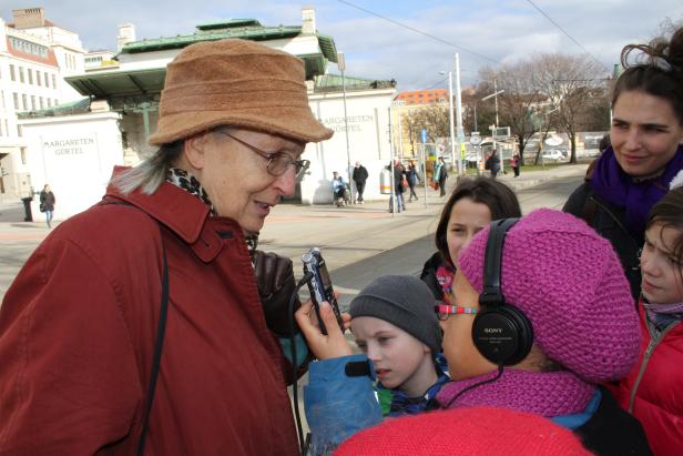 Eine ältere Frau interviewt Kinder am Margareten Gürtel in Wien mit einem Aufnahmegerät.