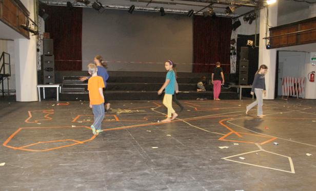 Kinder bewegen sich auf einer Bühne mit aufgezeichneten Linien.