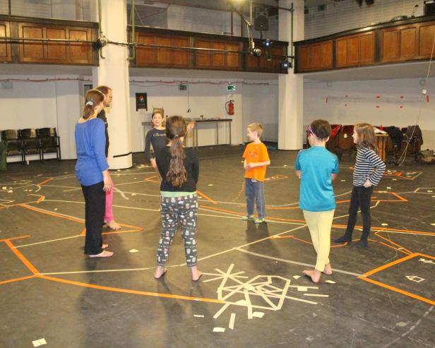 Eine Gruppe von Kindern und ein Erwachsener stehen barfuß in einem Raum mit Linien auf dem Boden.