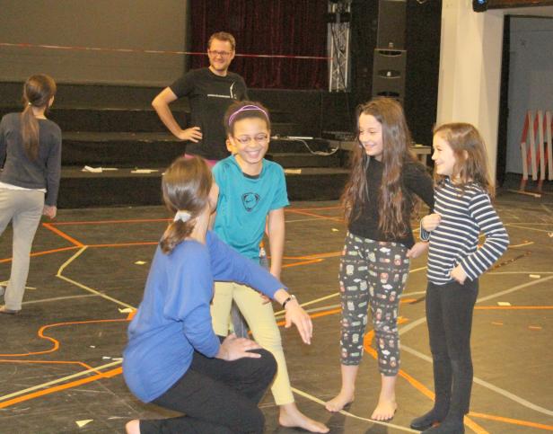 Eine Gruppe von Mädchen und ein Mann stehen auf einer Bühne mit Linien auf dem Boden.