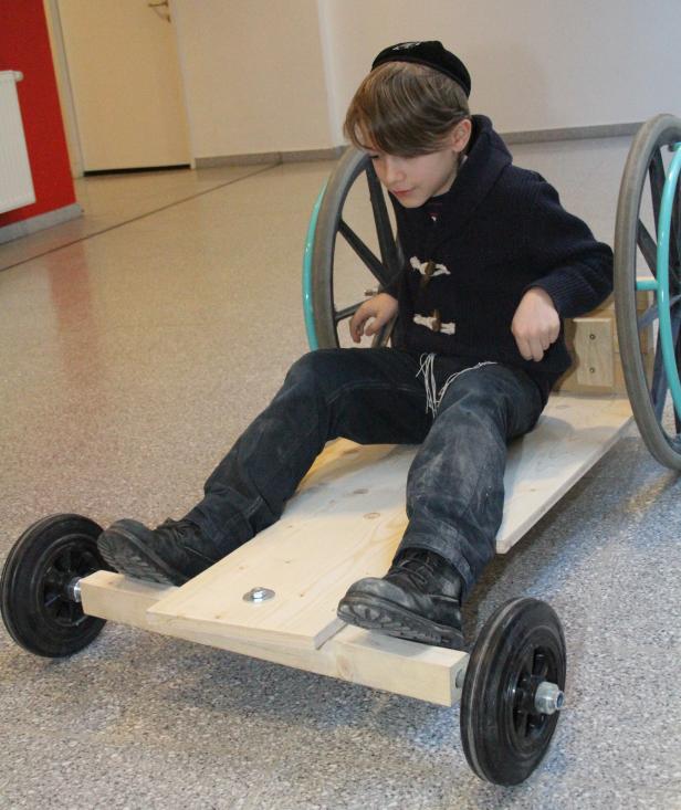 Ein Junge sitzt auf einem selbstgebauten hölzernen Seifenkistenfahrzeug.