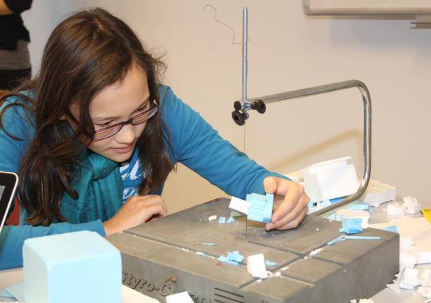 Ein Mädchen mit Brille schneidet Styropor mit einem Schneidegerät.