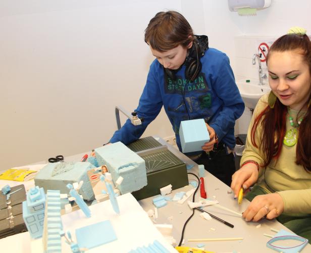 Ein Junge und eine Frau basteln an einem Tisch mit hellblauem Styropor an einem Modell.