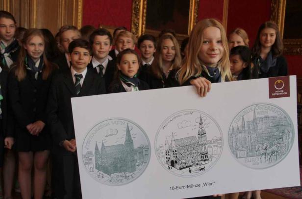Eine Gruppe von Kindern hält eine Tafel mit Abbildungen von 10-Euro-Münzen „Wien“.