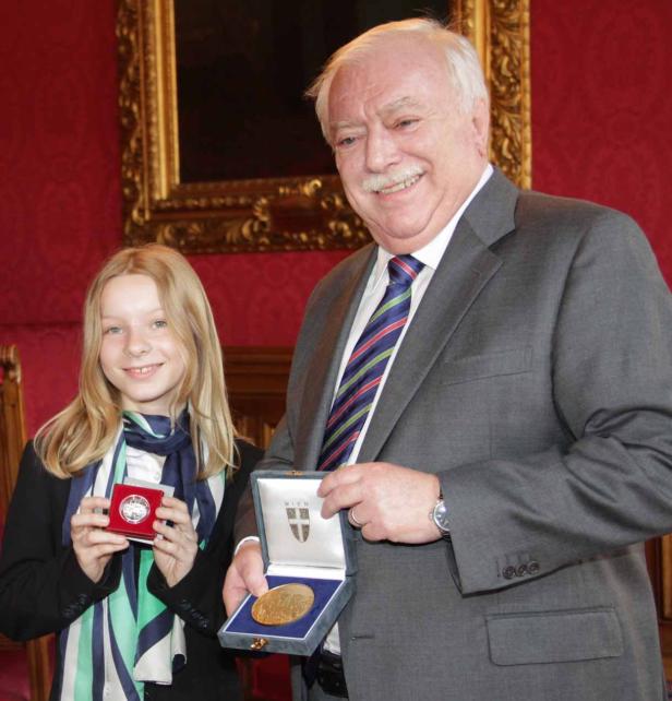 Ein Mann im Anzug und ein junges Mädchen halten Medaillen in ihren Händen.