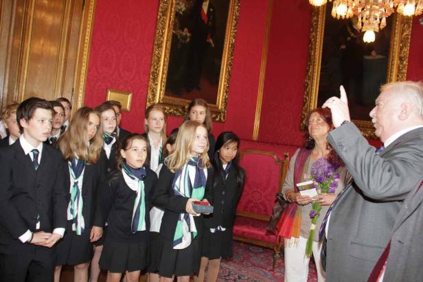 Eine Gruppe von Schülern in Uniform wird von zwei Erwachsenen in einem formellen Raum empfangen.