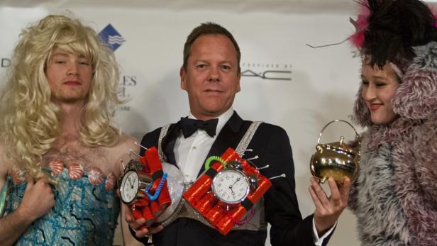 Kiefer Sutherland posiert mit zwei verkleideten Personen und hält Requisiten in der Hand.
