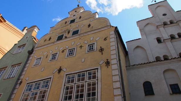 Die Fassaden von drei historischen Gebäuden in Riga unter blauem Himmel.