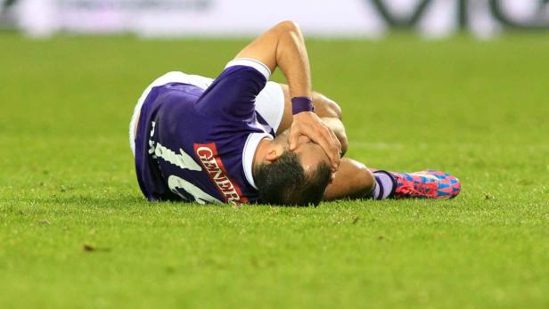 Ein Fußballspieler liegt verletzt auf dem Rasen und hält sich den Kopf.