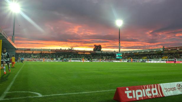 Ein Fußballstadion bei Sonnenuntergang mit Zuschauern auf den Tribünen.