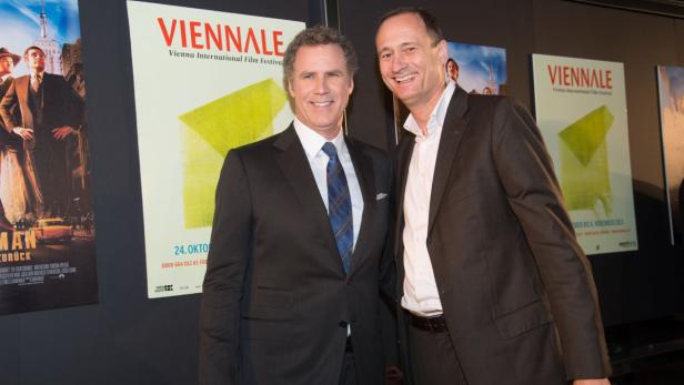 Will Ferrell und ein Mann im Anzug posieren vor Postern der Viennale.