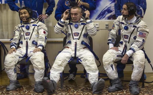 Drei Astronauten sitzen in ihren Raumanzügen nebeneinander.