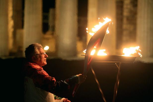 Ein Mann hält eine brennende Fackel vor einem Altar mit einer Flamme.