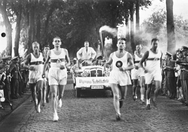 Läufer tragen die olympische Fackel durch eine Menschenmenge.