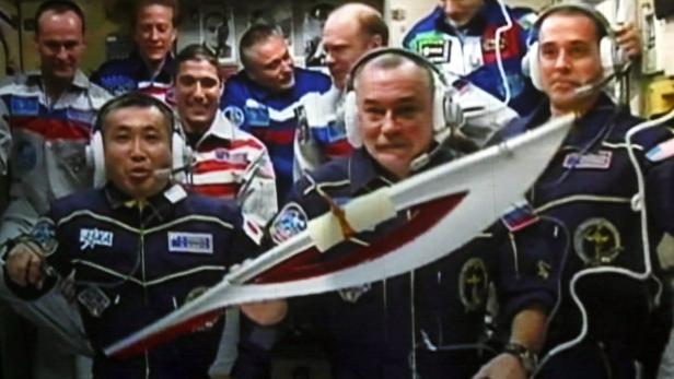 Eine Gruppe von Astronauten posiert mit einem zeremoniellen Schwert im Weltraum.