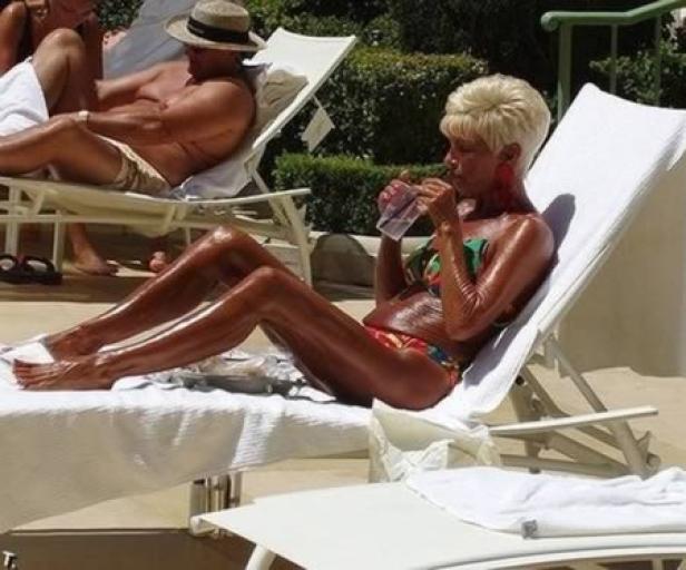 Eine Frau mit blonden Haaren liegt auf einer Liege und trinkt etwas.