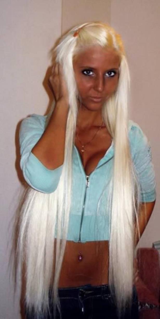 Eine Frau mit platinblondem, langem Haar und stark gebräunter Haut posiert.