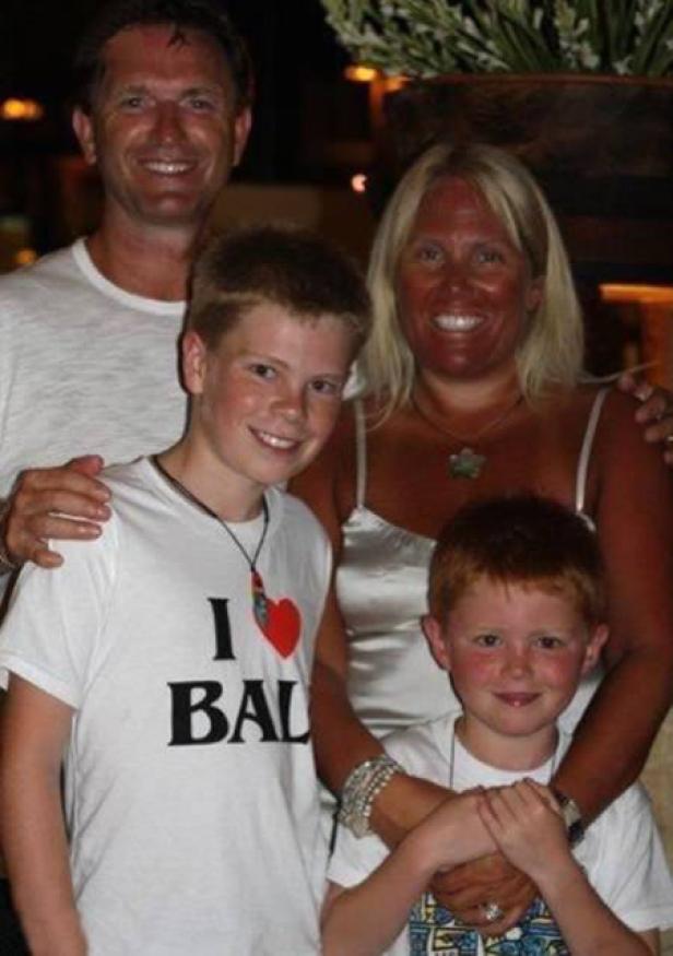 Eine Familie posiert lächelnd für ein Foto. Ein Junge trägt ein T-Shirt mit der Aufschrift „I <3 BALI“.