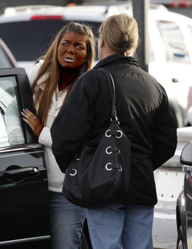 Eine Frau mit stark gebräunter Haut spricht mit einer anderen Person neben einem Auto.