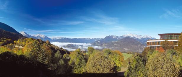 Panoramaaufnahme einer herbstlichen Berglandschaft mit einem modernen Gebäude im Vordergrund.