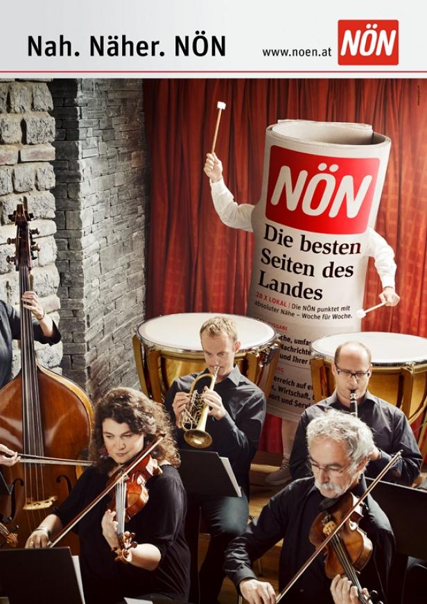 Ein Orchester spielt, während eine Person im NÖN-Zeitungskostüm dirigiert.